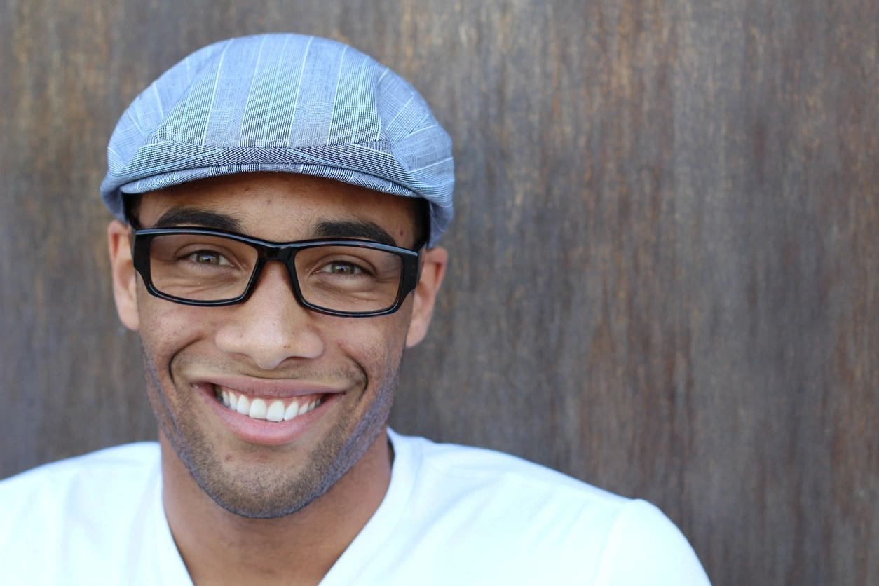 A man with glasses and a hat smiling.